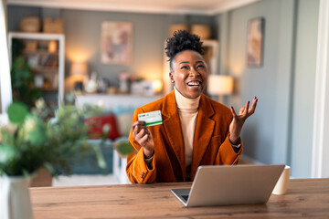 Excited young businesswoman, satisfied buyer holding credit card, using online bank app on laptop making convenient financial e-commerce payment digital transaction at home office.