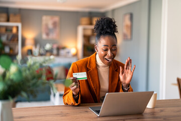 Excited woman hand gesturing while using laptop and credit card at home.