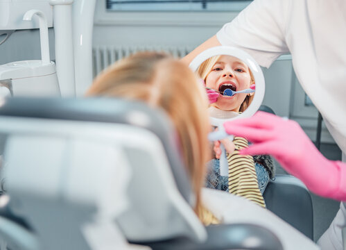 Little girl looking at mirror while dentist doctor doing teeth prevention with excavator and mirror medical tools in stomatology clinic. Healthcare, kid's health and medicare industry concept image.