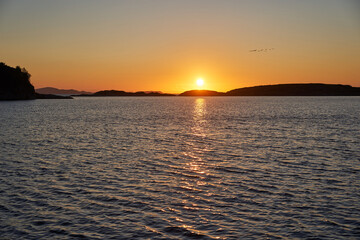 Landscape picture of the midnight sun in golden hour over the Norwegian sea with small islands at...