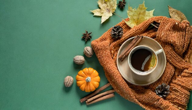 crisp fall morning aesthetic from top view brown knitted sweater a hot coffee cup raw pattypans acorn cinnamon sticks maple leaves dried orange slice on green backdrop offering space for text