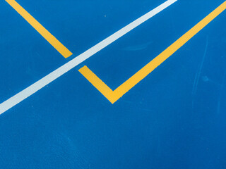 Close up photo of a outdoor blue tennis court with white lines combined with yellow, gold, pickleball lines.	