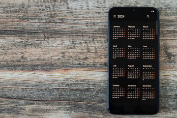 Digital calendar 2024 year on smartphone screen placed on wooden desk. Top view, copy space. Modern...