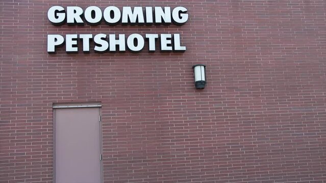 grooming petshotel writing caption text sign in white lettering mounted to brick wall above door and exterior light outside exterior outdoors