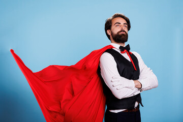 Powerful superhero wears red cape and feeling strong to save citizens, posing against blue...