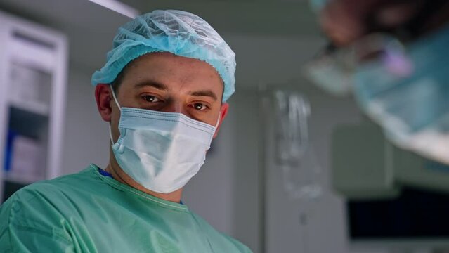 Caucasian brunet male doctor in mask and cap. Portrait of a mid-aged surgeon at blurred backdrop. Close up.