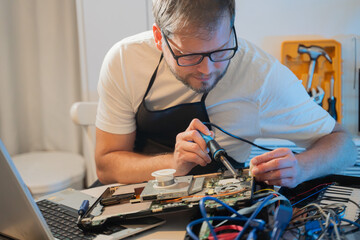 a man repairman makes repairs and soldering irons electronics in a laptop in a home appliance...