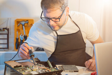 a man repairman makes repairs and soldering irons electronics in a laptop in a home appliance...