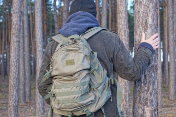 one green army backpack on the back of a man in a black hat and gray jacket on an autumn street