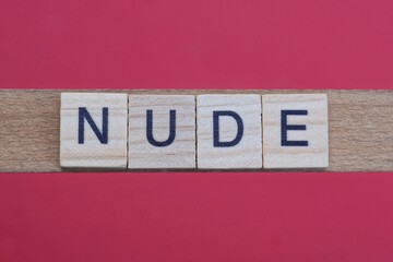 text the word nude from gray wooden small letters with black font on an red table
