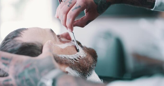 Shave, foam or grooming with a barber and man in a seat as a customer for luxury or professional service. Face, beard or salon and the hands of a person shaving a client with a minora blade closeup