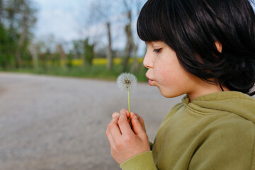 side view of child with freckles in green top blowing a dandelion outdoors