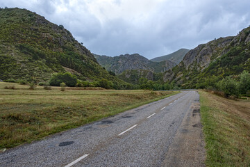 Fototapeta premium Beautiful landscape photo of road going through natural park full of mountains and trees during summer in cordillera Cantabrica, picos da europa, leon, asturias, spain