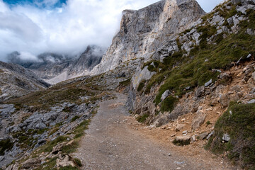 Huge beautiful gray mountain range with hiking trail path in sunny day with clouds during summer in cordillera Cantbrica, picos da europa, leon, asturias, spain