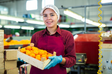 Happy young female worker of citrus sorting factory showing ripe selected mandarin oranges packed in wooden box © JackF