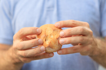 Guy's hand holds a round bun, snack and fast food concept. Selective focus on hands with blurred background