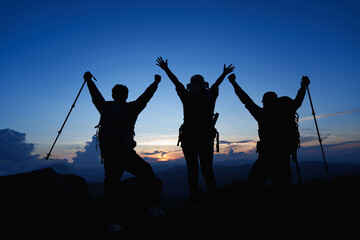Silhouette of Asian three people standing raised hands with trekking poles and kerosene black lamp...