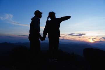 Silhouettes of Happy family father, mother and child daughter for hand and looking stands on the cliff and looks at the tops of mountains and watching the sunrise. Family with small children hiking