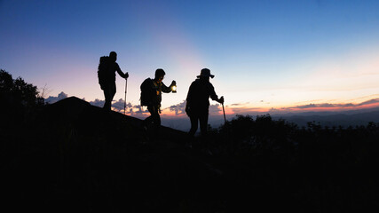 Silhouette of Asian teamwork hikers climbing up mountain cliff and one of them giving helping hand...