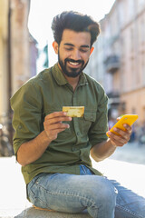 Indian man using credit bank card smartphone while transferring money, purchases online shopping,...
