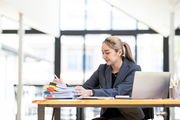 Asian Business woman using calculator and laptop for doing math finance on an office desk, tax, report, accounting, statistics, and analytical research concept
