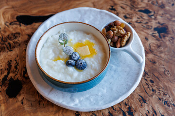 Milk rice porridge with blueberry, butter, nuts and mint leaf, creamy rice pudding or french riz au lait in a ceramic bowl on wooden table. Top view