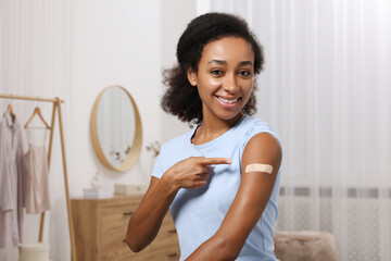 Happy young woman pointing at adhesive bandage after vaccination indoors - obrazy, fototapety, plakaty