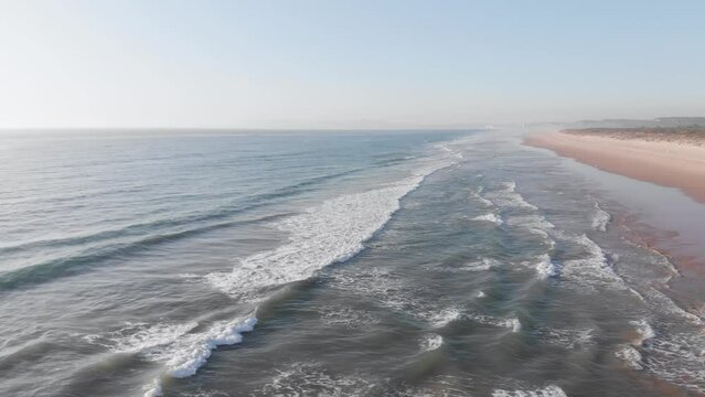 Relaxing aerial footage capturing the gentle approach of ocean waves to a vast sandy beach. Serene and soothing nature scene from an elevated perspective.