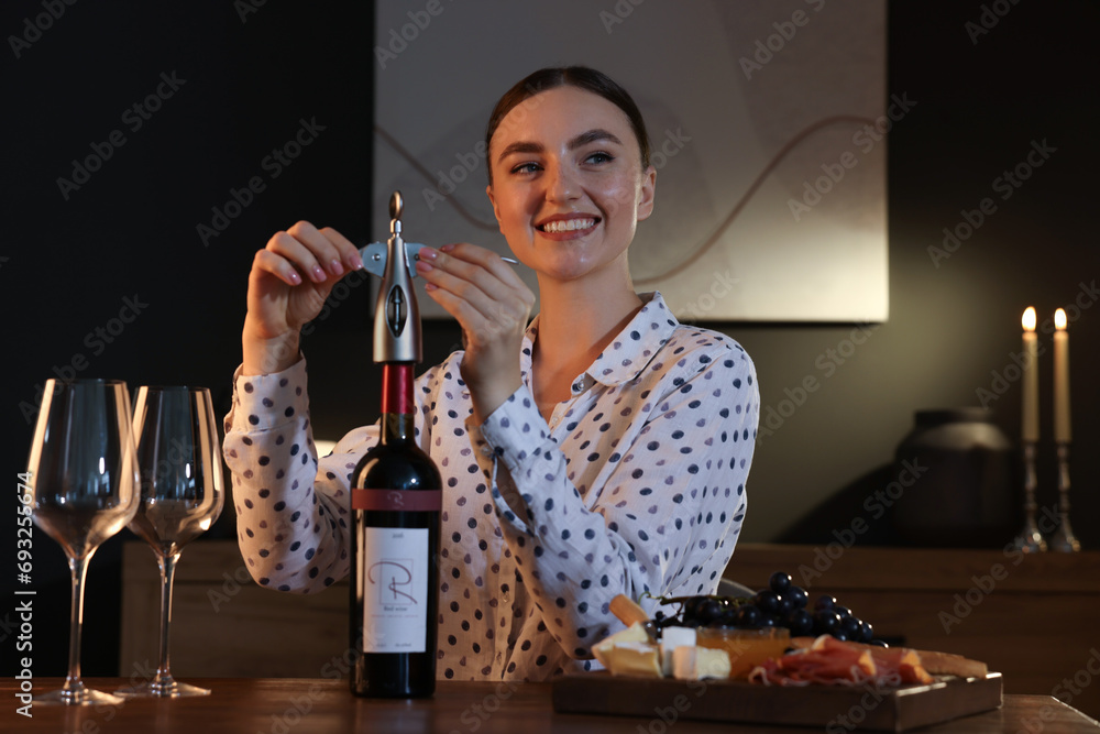 Canvas Prints Romantic dinner. Happy woman opening wine bottle with corkscrew at table indoors