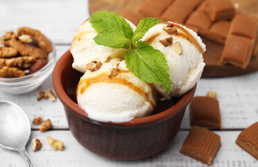 Bowl of tasty ice cream with caramel sauce, mint and nuts on white wooden table, closeup