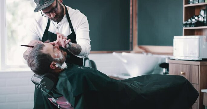 Beard, shaving foam and a barber with a man in a seat as a customer for luxury or professional service. Salon, shave or hairdresser and a person grooming the face of a client with a minora blade