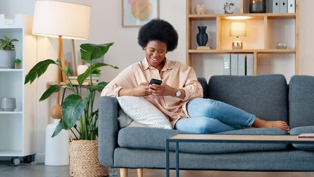 Laughing afro woman streaming on phone, watching funny comedy videos online on a subscription movie channel. Smiling, happy woman sitting on home living room sofa, relaxing and browsing social media