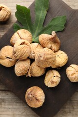 Board with tasty dried figs and green leaf on wooden table, flat lay