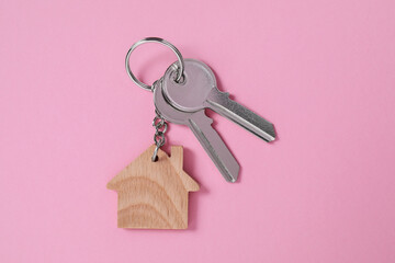 Metallic keys with wooden keychain in shape of house on pink background, top view