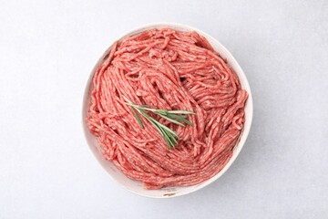 Fresh raw ground meat and rosemary in bowl on light table, top view