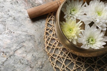 Tibetan singing bowl with water, beautiful chrysanthemum flowers and mallet on table, above view....
