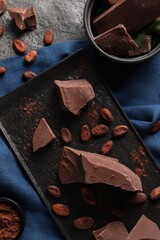 Pieces of tasty milk chocolate, cocoa beans and powder on grey table, top view