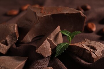Pieces of tasty milk chocolate and mint on table, closeup