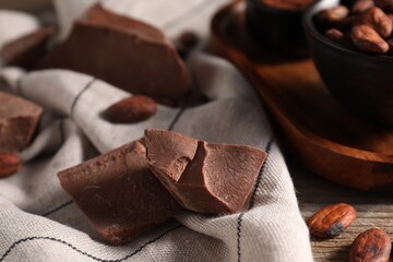 Pieces of tasty milk chocolate and cocoa beans on table, closeup
