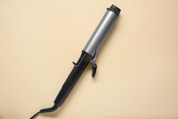Hair curling iron on beige background, top view