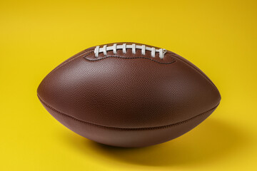 Brown leather American football ball on yellow background, closeup