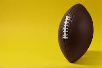 American football ball on yellow background, space for text