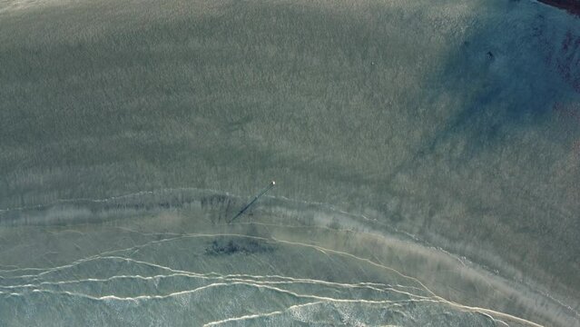 Aerial view above sandy beach with a person walking alone at sunset next to the waves with their long shadow on the sand