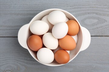 Unpeeled boiled eggs in saucepan on grey wooden table, top view