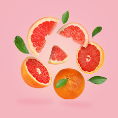 Cut and whole grapefruits and green leaves falling on pink background