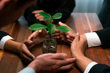 Business people holding money savings jar together in synergy filled with coin and growing plant...
