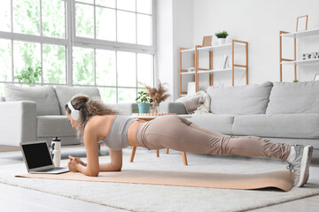 Sporty adult woman training on yoga mat while watching online tutorials at home
