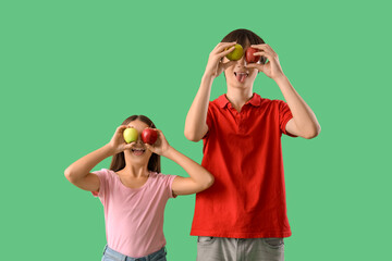 Cute girl and her brother with fresh apples showing tongues on green background