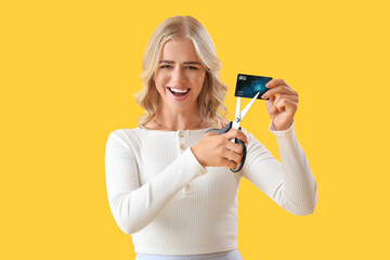 Young woman cutting credit card on yellow background - obrazy, fototapety, plakaty