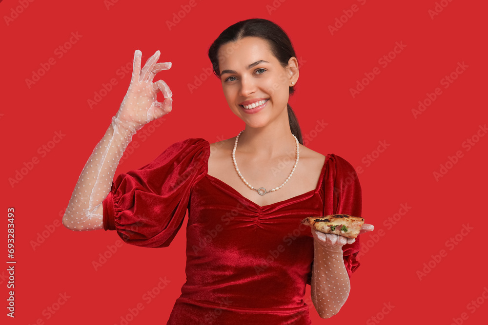 Poster Beautiful young woman with slice of tasty pizza showing OK gesture on red background